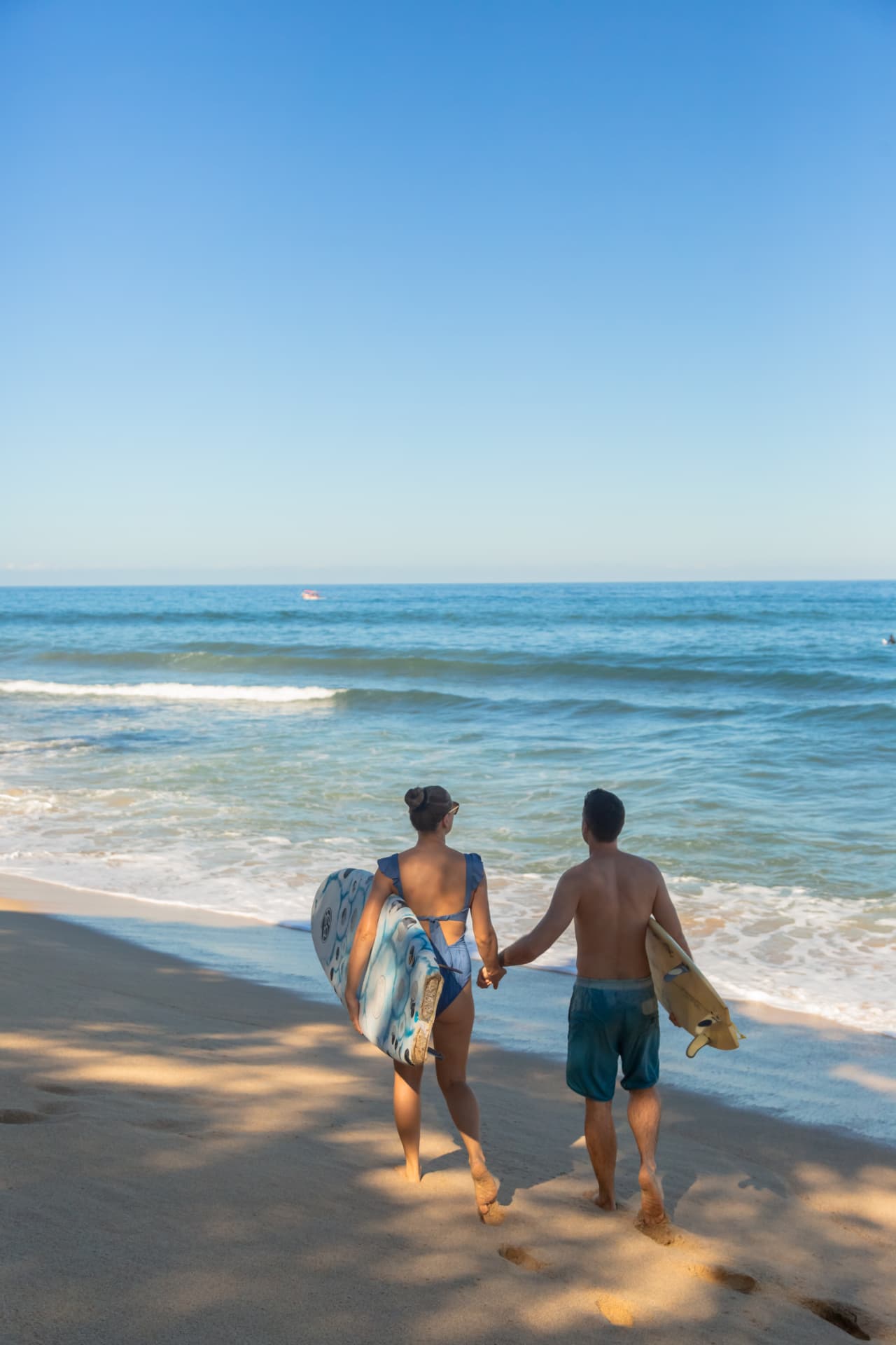 Pareja caminando hacia el mar con tablas de surf frente a Amaca Beach Retreat