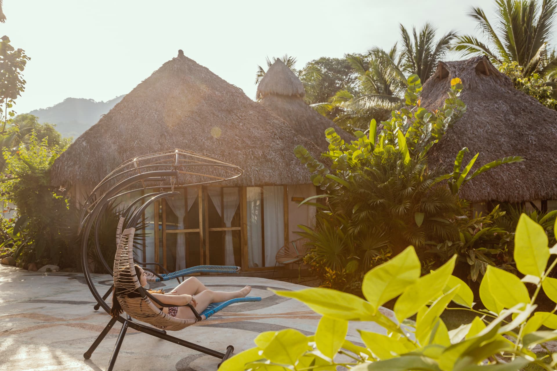 Woman resting on a hanging lounger in front of the hotel palapas