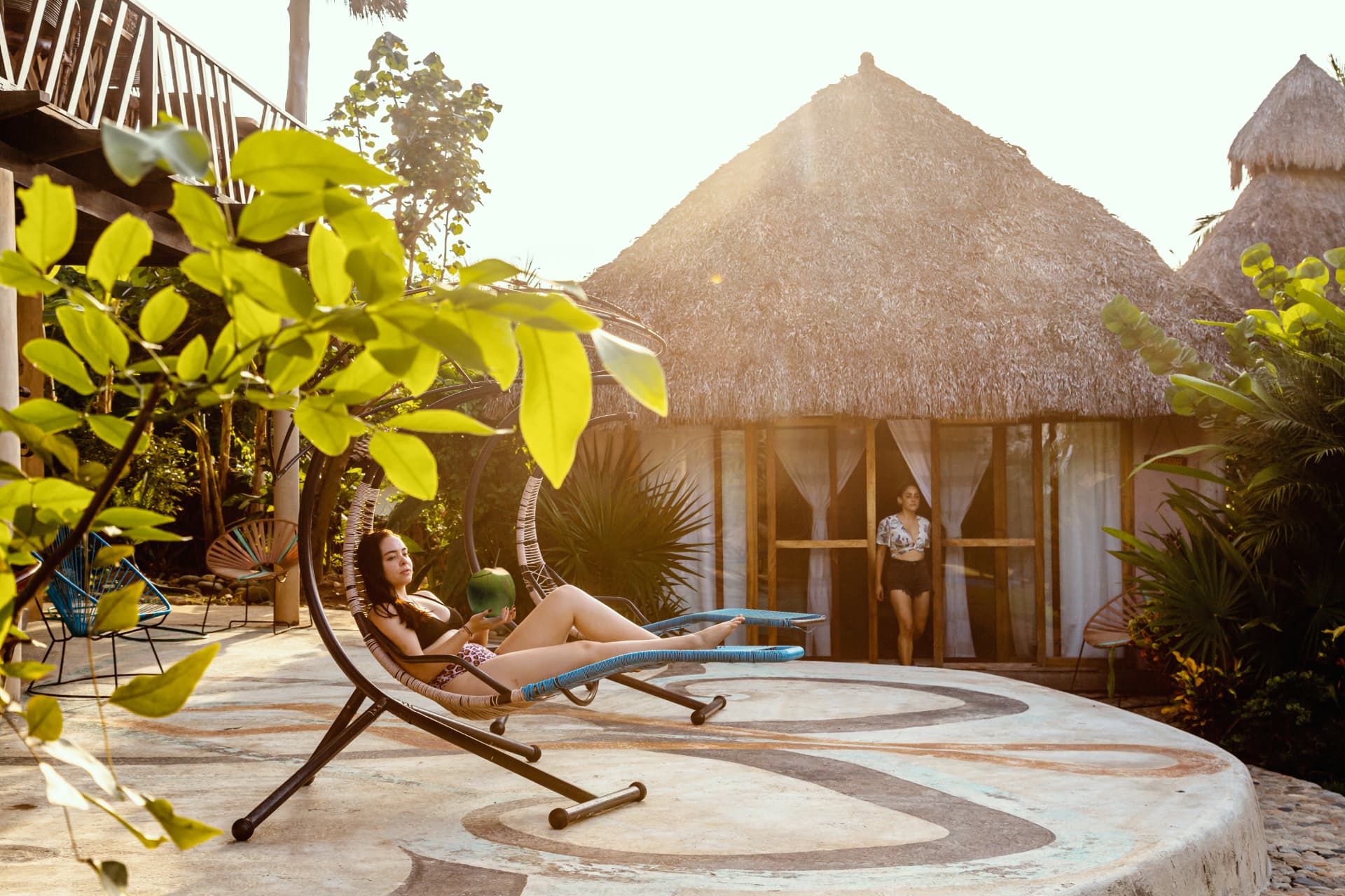 Woman with a fresh coconut on the hanging lounger at sunset