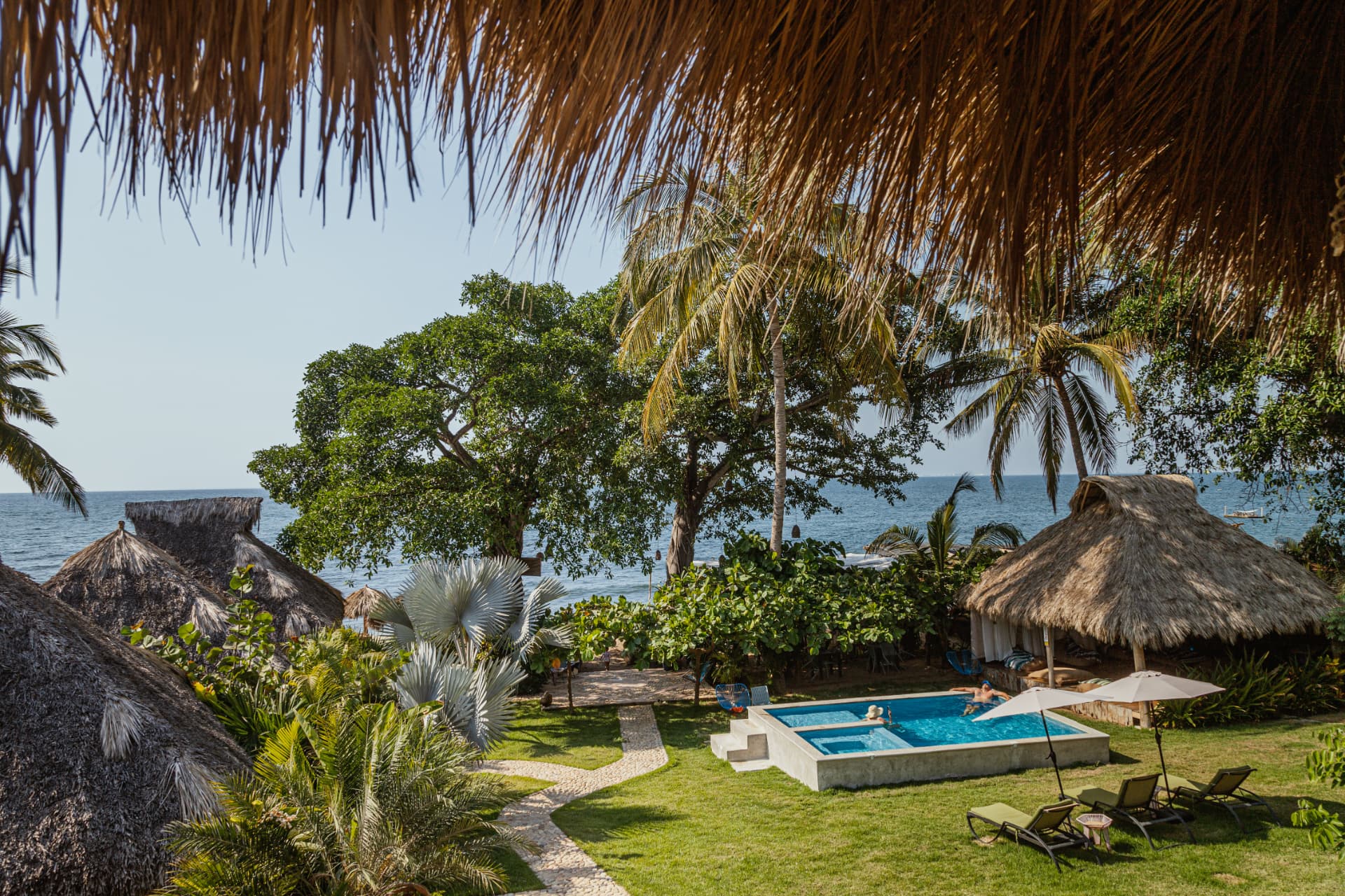 Oceanfront pool surrounded by palapas and garden at Amaca Beach