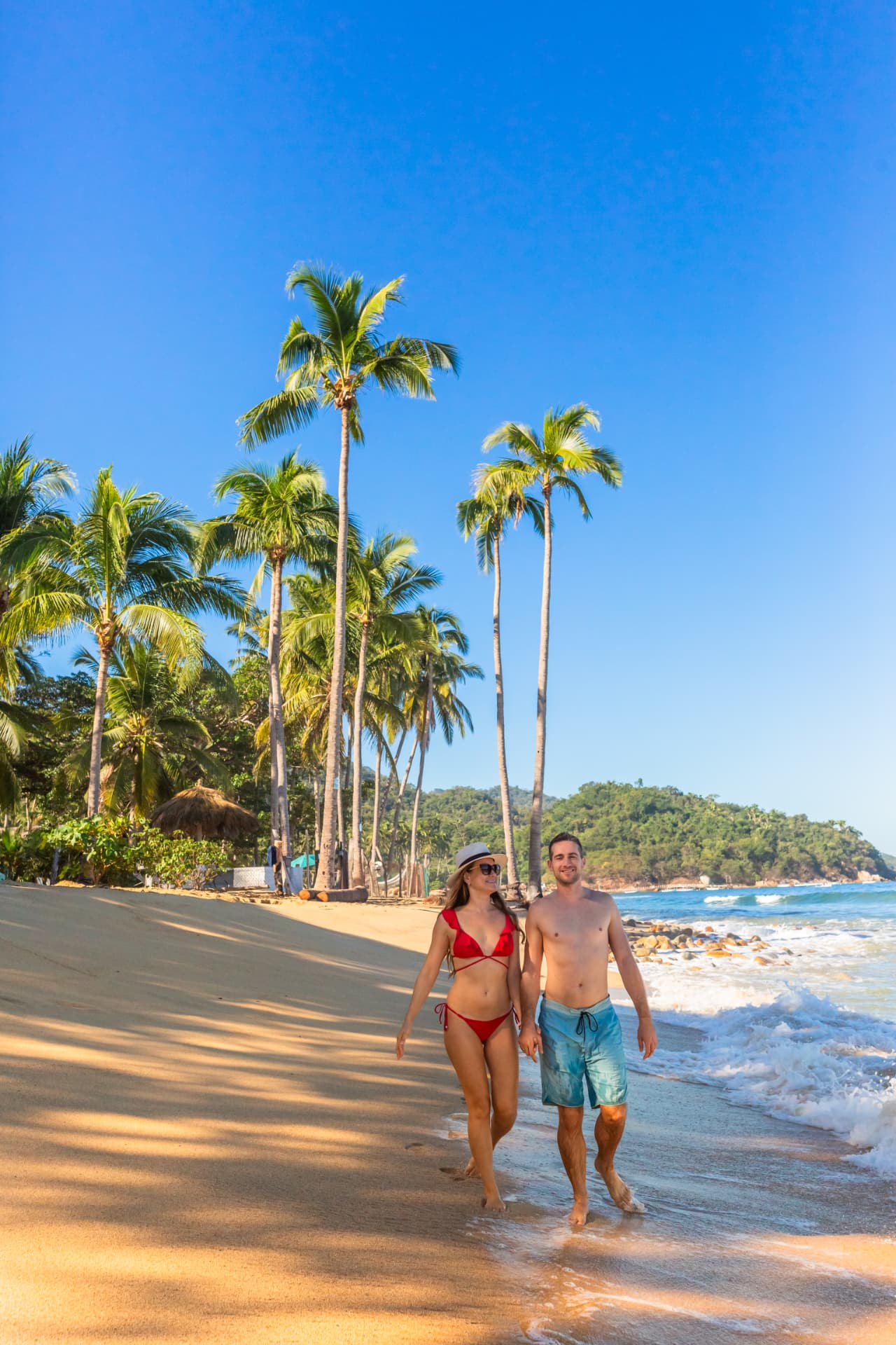 Couple walking the shoreline under the tall palms of Quimixto