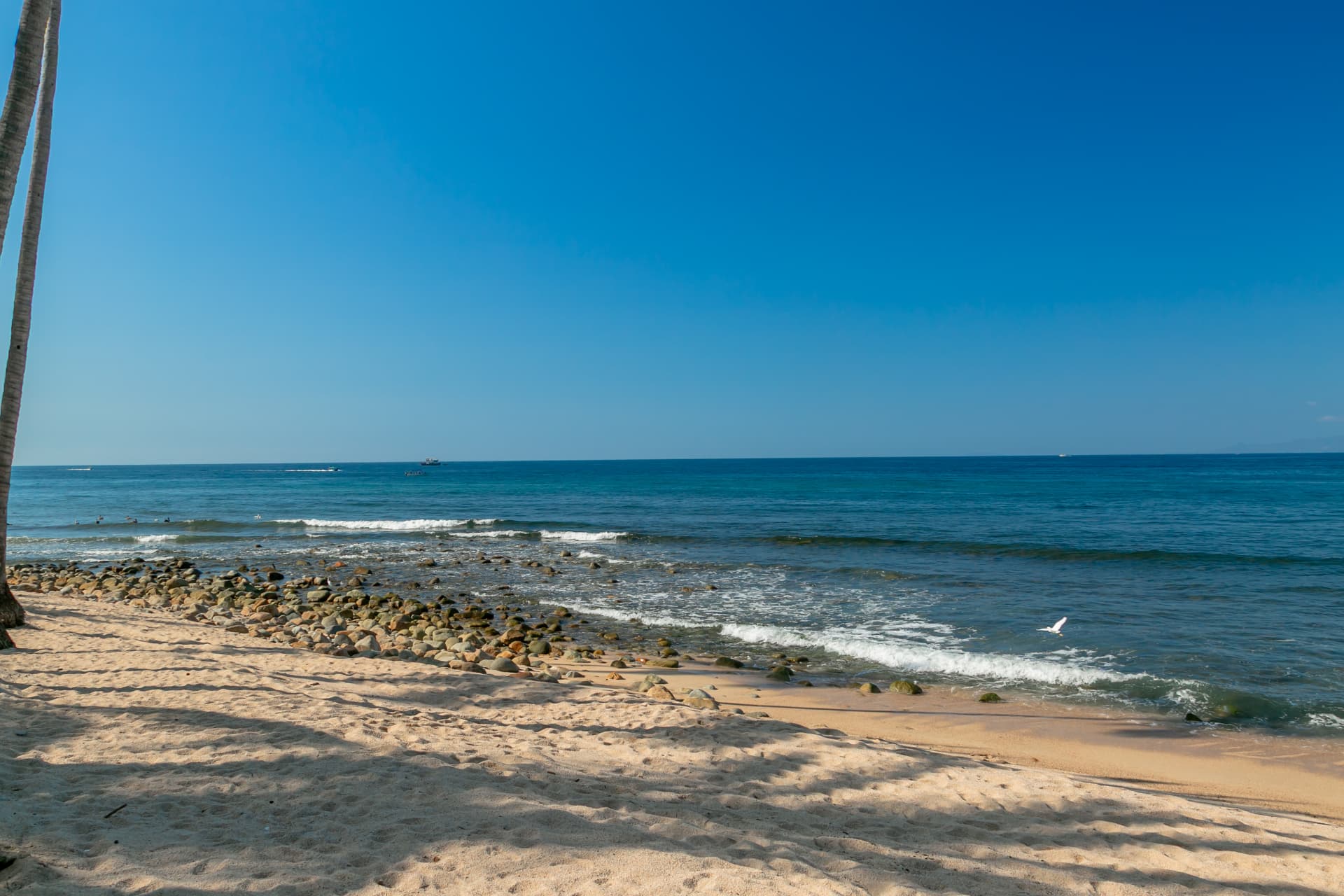 Golden sand beach with river stones and deep blue sea under a clear sky