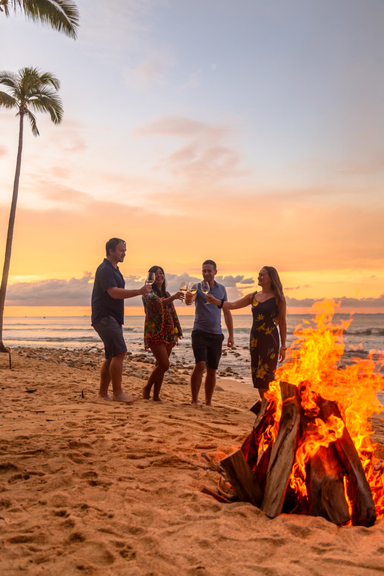 Group of friends toasting by the beach bonfire at sunset