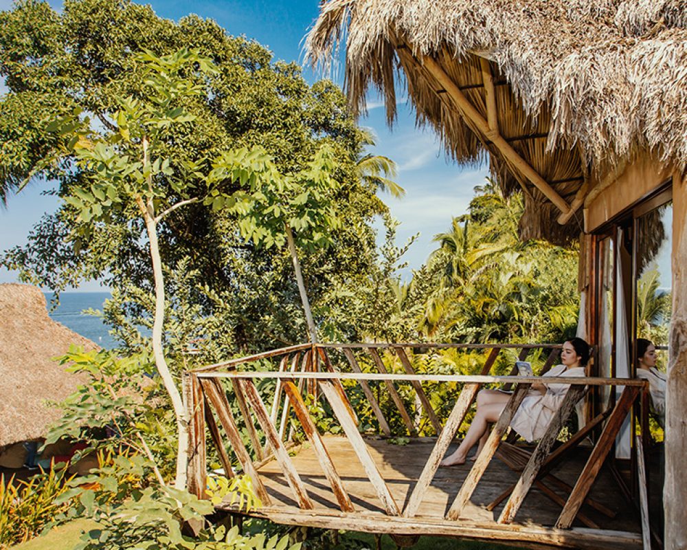 Mujer relajándose en el balcón superior de una habitación privada con vista panorámica al mar tropical.